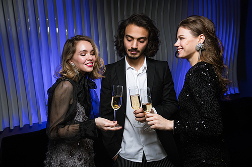 Three young elegant friends cheering up with flutes of champagne at party during celebration in night club