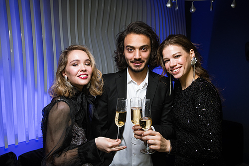 Young man in suit standing between two beautiful girls during new year toast at party in night club