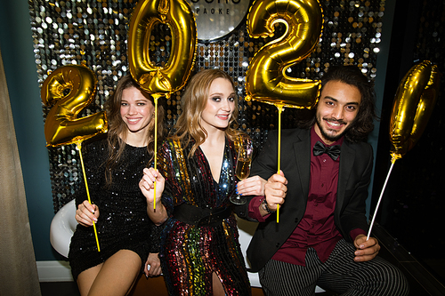 Three young friends in glamorous attire holding golden inflatable numbers of the following year at party