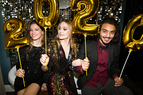 Three happy young friends holding golden inflatable numbers of the following year while having fun at party