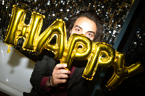 Young cheerful man holding golden inflatable balloon letters by his face while having fun at party in the night club
