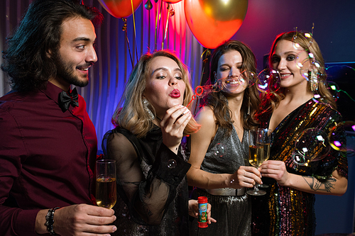 Blond pretty girl blowing soap bubbles among her friends while enjoying birthday party in the night club