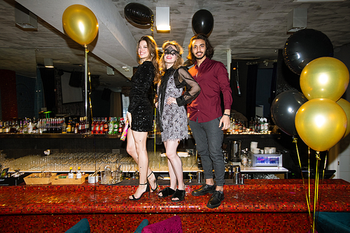 Two pretty girls and elegant guy standing on counter in luxurious restaurant or night club during celebration of new year