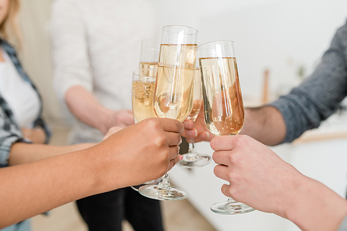 Hands of young multiracial friends clinking with flutes of sparkling champagne while toasting for new year or other holiday at party