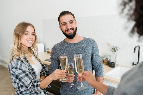 Happy young casual couple with flutes of champagne toasting with one of their friends at home party