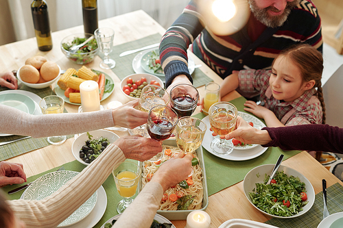 Hands of family of six clinking with drinks over festive table homemade food during Thanksgiving dinner at home