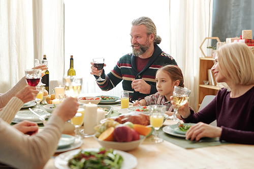 Happy senior man holding glass of wine over served table during Thanksgiving toast at festive family dinner