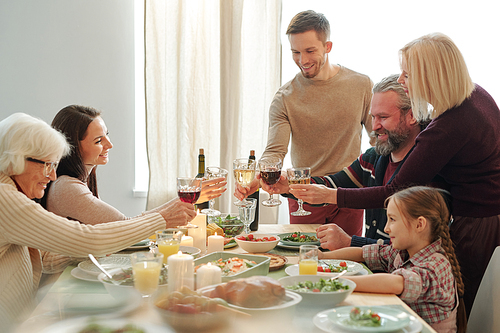 Happy mature and young family members clinking with wine during Christmas toast served festive table at dinner