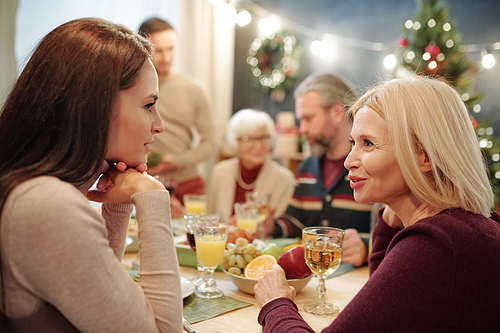 Young and mature women discussing something by served festive table during family dinner on Christmas eve