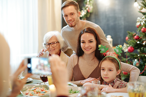 Happy family sitting by served festive table and  in smartphone held by female in front of them