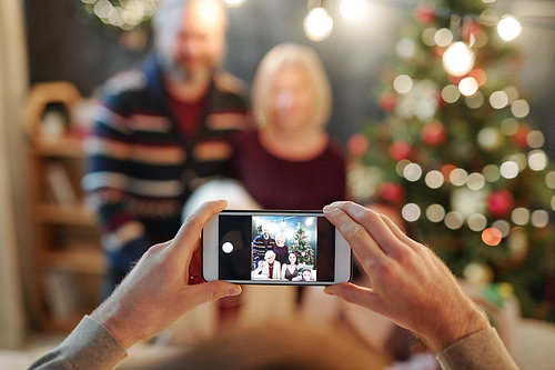 Hands of man holding smartphone while taking photo of big relaxed family by festive dinner on Christmas eve
