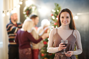 Happy young brunette woman with glass of wine congratulating you on merry Christmas with her family on background