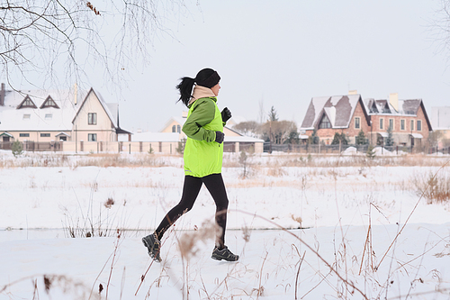 Young sporty woman with ponytail running close to countryside houses while training in winter