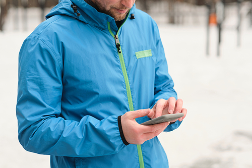 Close-up of man in blue jacket standing outdoors and using smartphone while watching video with exercise for training