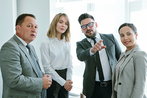 Confident mature businessman pointing forwards while standing among intercultural colleagues during discussion at meeting in office