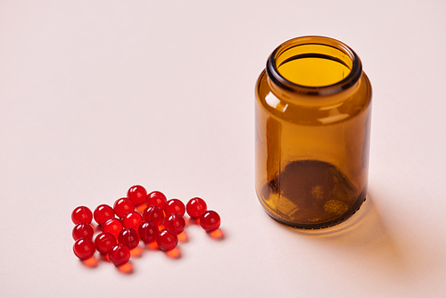Brown glass vitamin bottle and red vitamin drugs on pale pink surface, horizontal shot