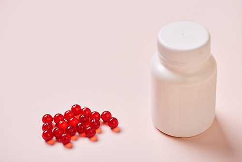 White plastic vitamin bottle and red vitamin drugs on pale pink surface, horizontal shot