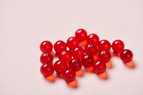 Bright red vitamin drugs on pale pink surface, horizontal close up shot