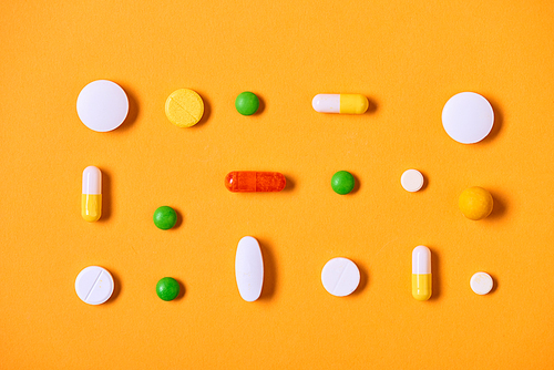 Multi-coloured medicaments on yellow background horizontal flat lay pattern shot