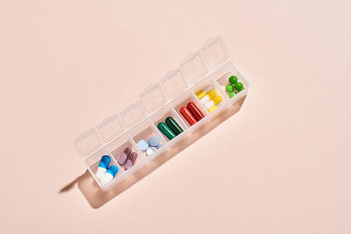 From above horizontal shot of portable plastic container for drugs with medicaments in it on pale pink background