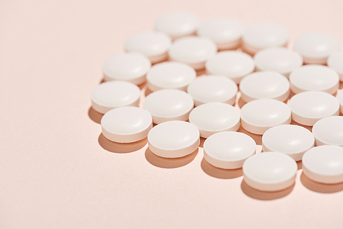 White pills of same shape on pale pink background horizontal close up shot