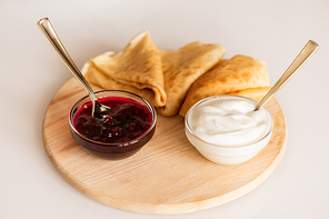Two small glass bowls with homemade cherry jam and sourcream and three hot appetizing folded on wooden board