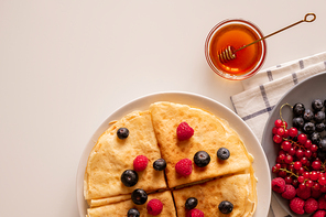 flatlay of kitchen table with appetizing homemade crepe with fresh berries on plate, small glass bowl with honey and folded napkin