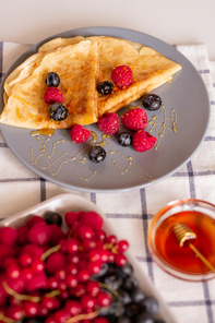 plate with two folded appetizing crepe with honey and fresh raspberries and blackberries on kitchen table served for breakfast