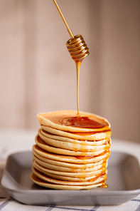 Fresh tasty honey being poured on top of appetizing homemade pancake stack on plate during process of cooking breakfast