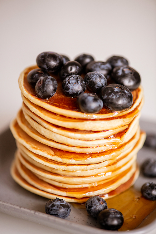 Stack of appetizing pancakes with honey and blackberries on plate on served table cooked at home or in cafe for breakfast