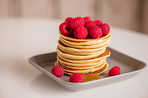 Fresh appetizing raspberries on top of stack of homemade hot pancakes with honey cooked for breakfast in the morning at home