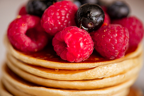 Macro image of hot appetizing homemade pancakes on plate with honey and mixture of fresh raspberries and blackberries on its top