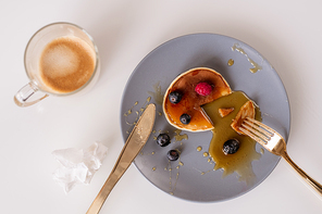 Top view of fork and knife on plate with appetizing homemade pancake with honey and fresh blackberries with mug of coffee standing near by
