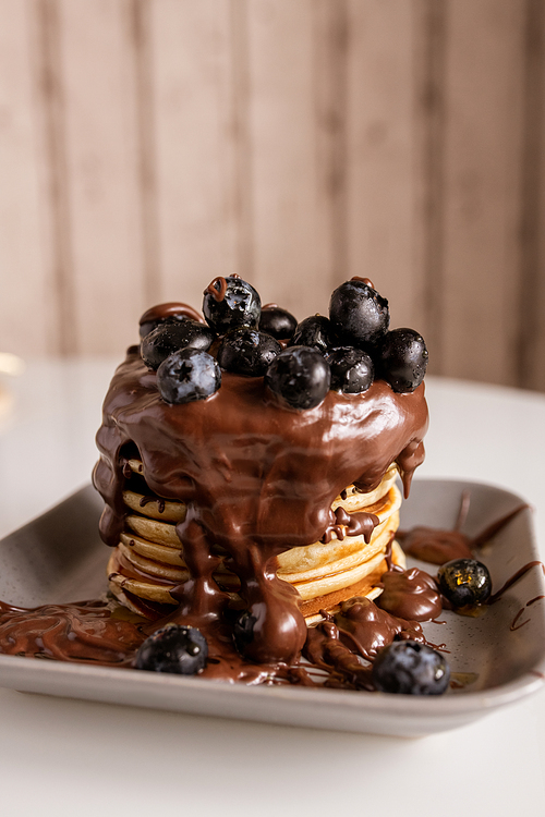 Stack of appetizing homemade pancakes with chocolate cream and fresh blackberries on its top on plate and on served kitchen table