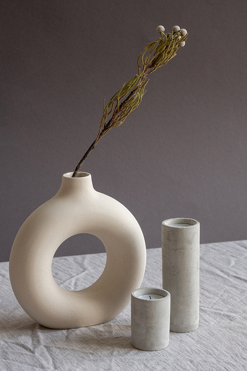 Composition of two aromatic blown out candles in white ceramic glasses standing on table by creative handmade vase with dried flowers