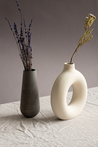 Still life composition with two ceramic handmade vases with dried lavender and wildflowers standing on table covered by white linen cloth