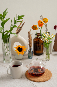 kitchen table with porcelain white mug, teapot with 홍차, group of various flowers and dried wildflowers in vases standing against wall