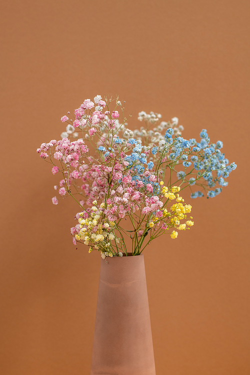 Bouquet of multi-color dried flowers in handmade clay vase standing on background of brown wall as a part of interior of domestic room