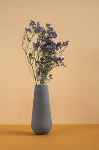 Bunch of blue dried wildflowers in grey clay or ceramic vase standing on table as decoration of domestic room or part of studio interior