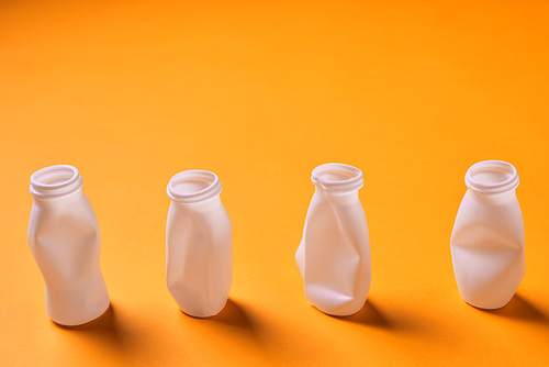 Four white disposable plastic bottles on orange background, conceptual studio horizontal shot