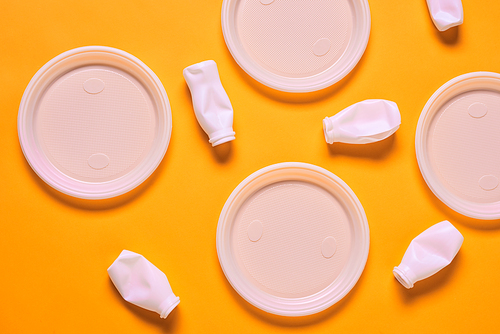 Horizontal from above flat lay shot of white plastic empty plates and bottles lying on orange surface