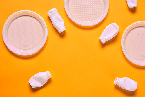 Horizontal flat lay composition of white plastic empty plates and bottles on orange background, copy space