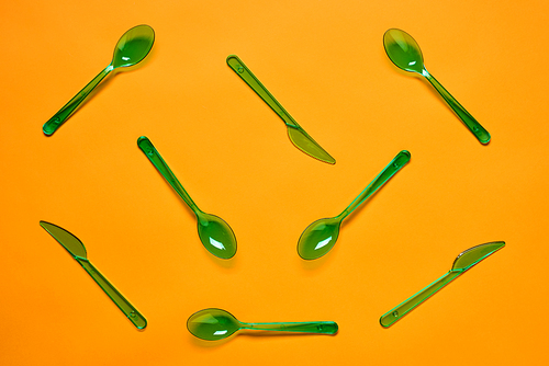 Horizontal flat lay conceptual pattern of green plastic spoons and forks on bright orange background