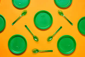 Horizontal flat lay conceptual shot of pattern made of green plastic plates and spoons on bright orange background