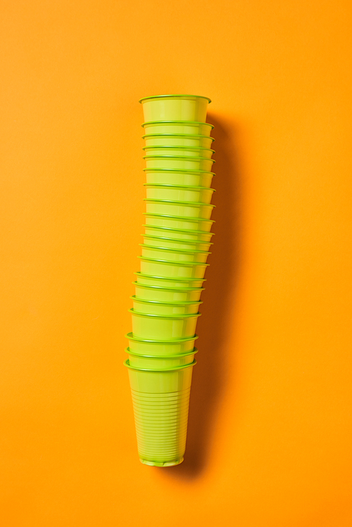 Vertical from above flat lay shot of disposable green plastic cups set on bright orange background