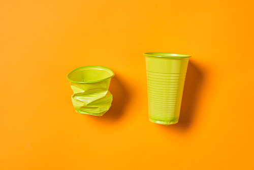 Horizontal from above flat lay shot of disposable used and new green plastic cups on bright orange background
