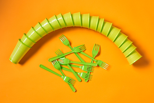 Conceptual flat lay shot of disposable light green plastic cups set and forks on bright orange background