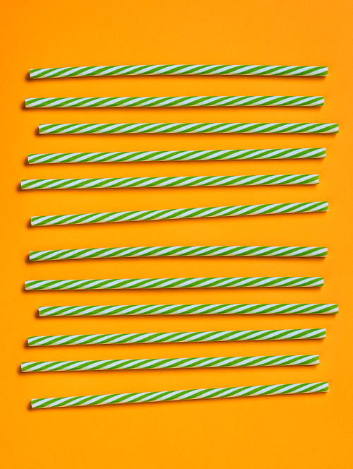 green and white striped plastic  straws on bright orange background, vertical flat lay shot