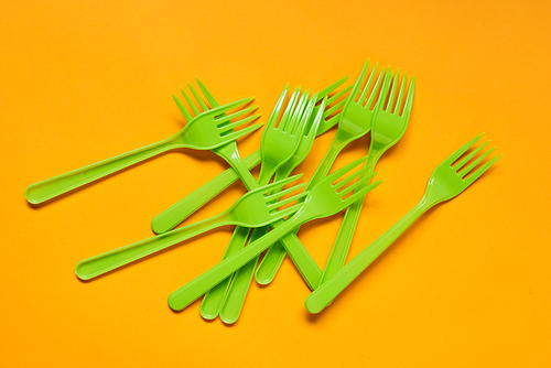 Disposable light green plastic forks lying on bright orange background, horizontal conceptual flat lay shot
