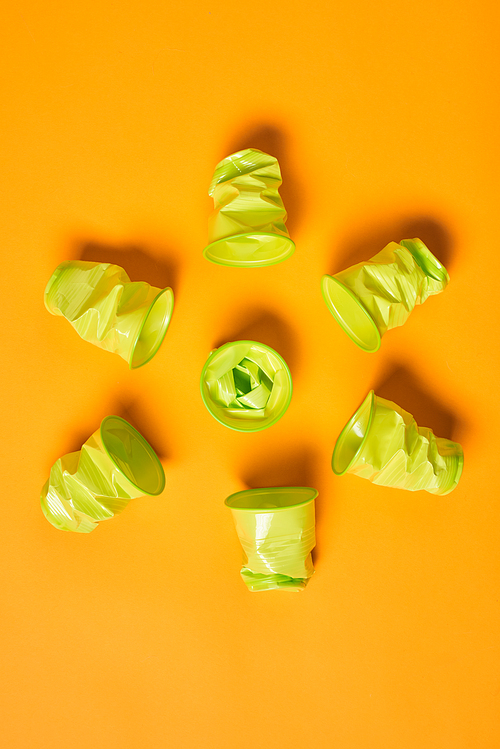 Vertical flat lay pattern shot of used light green plastic cups on bright orange background